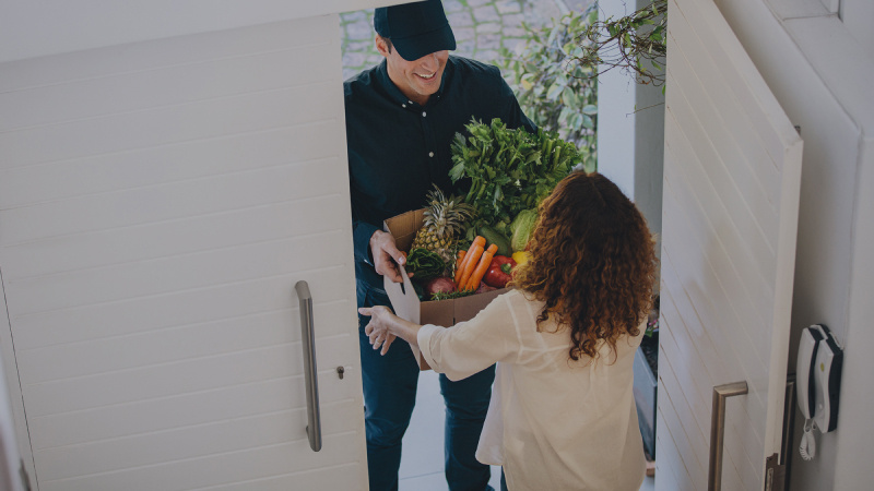 Woman receiving a box of vegetables from a delivery man