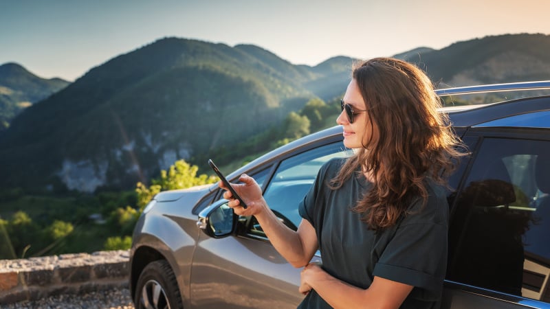 Woman using phone while resting on a car